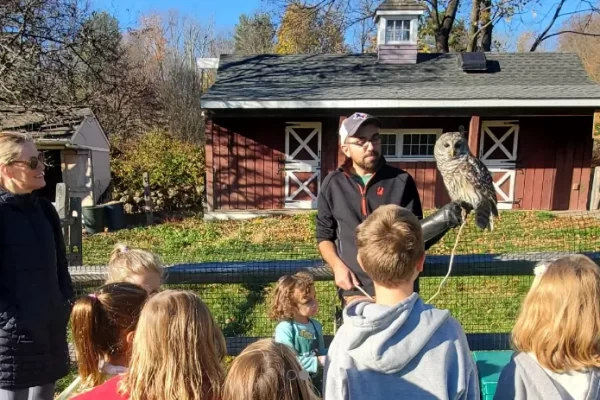 image of a man speaking while holding an owl with people looking on